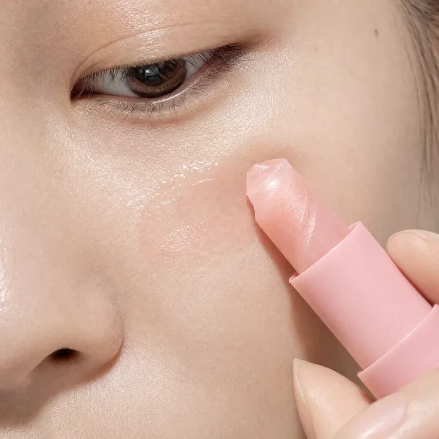 The pink balm tip touching the cheekbone with a glossy trail of balm on the skin