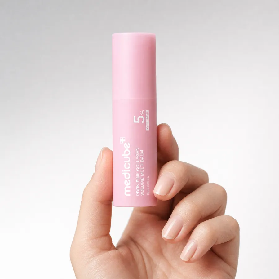 A hand holding the pink medicube balm stick upright against a soft white background, showing its size