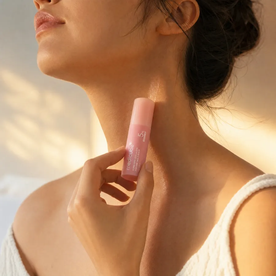 A woman drawing the pink medicube balm stick down the side of her neck in warm dappled sunlight
