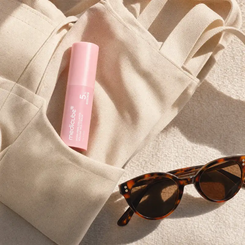 The medicube balm stick tucked into the pocket of a canvas tote bag beside a pair of sunglasses