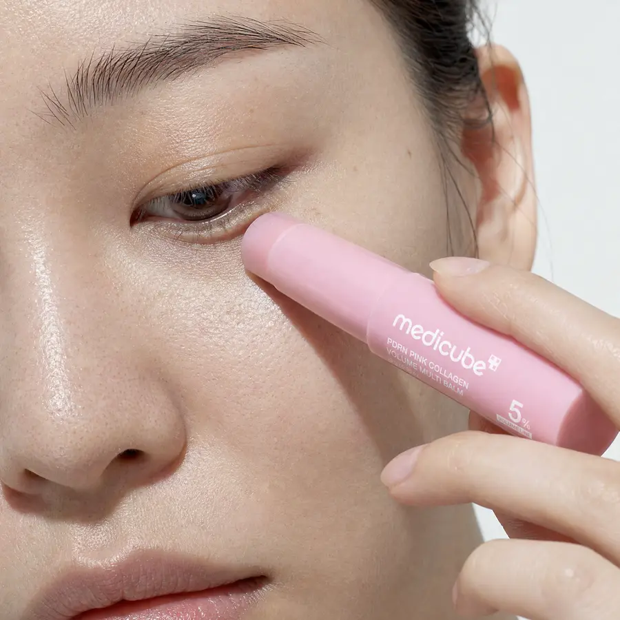 Close-up of a woman gliding the pink medicube balm stick along the skin under her eye
