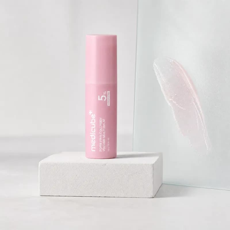 The medicube balm stick upright on a white plaster block beside a swatch of the balm on frosted glass