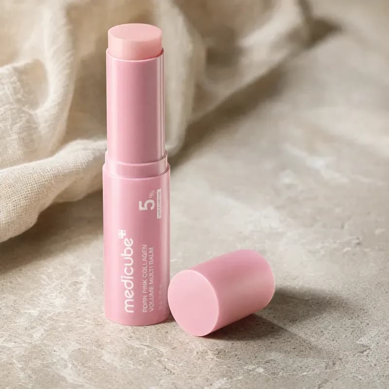 One medicube PDRN Pink Collagen Volume Multi Balm stick standing on travertine with its cap beside it