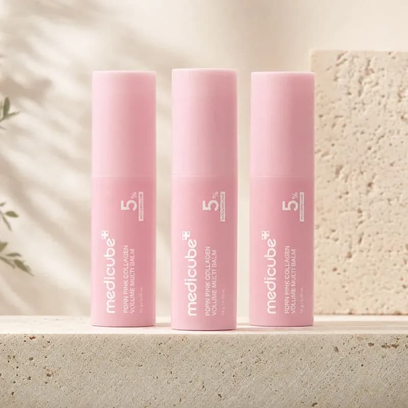 Three medicube PDRN Pink Collagen Volume Multi Balm sticks standing in a row on a travertine ledge