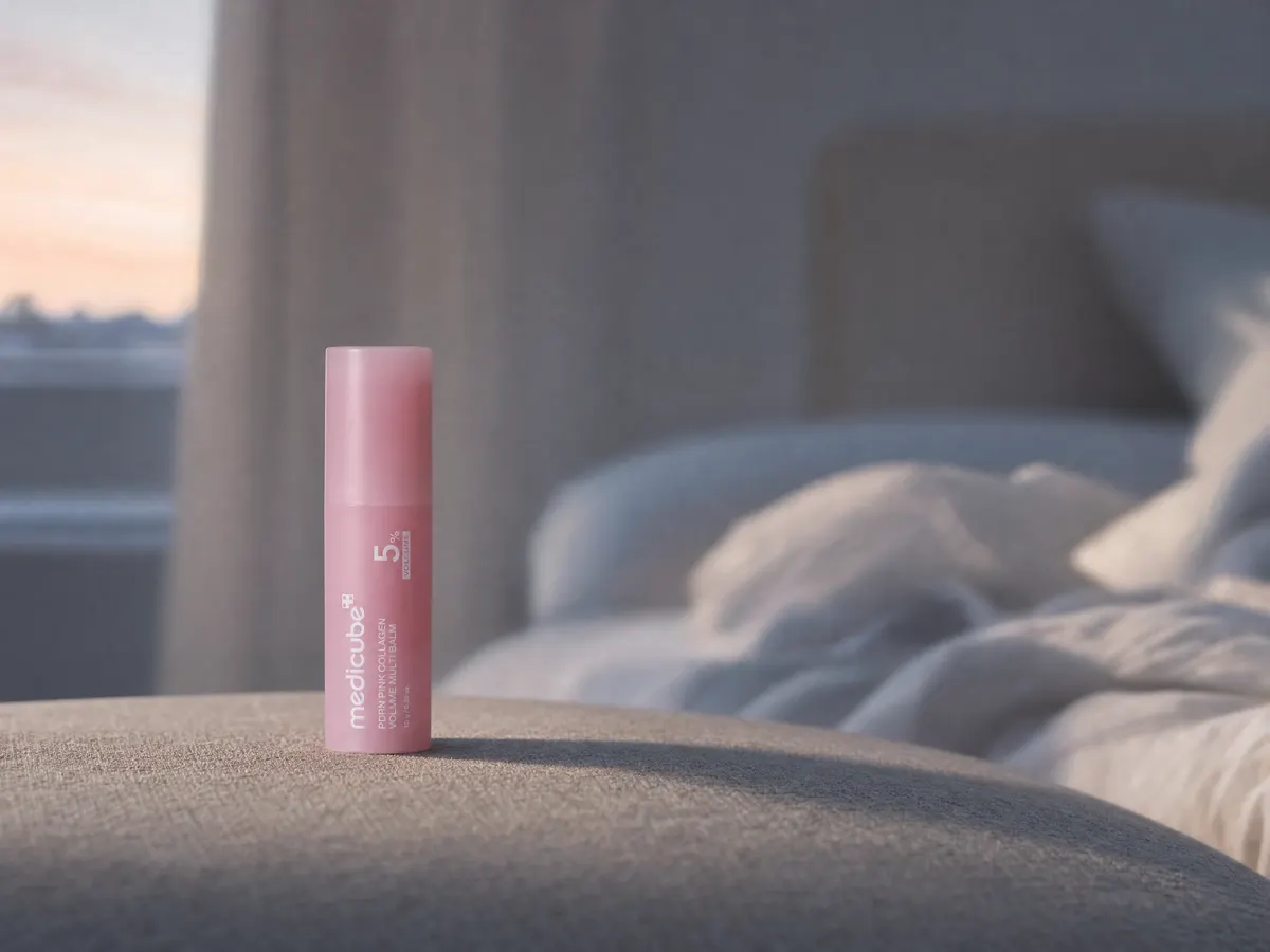 The medicube balm stick on a linen nightstand at dawn with a softly blurred bedroom behind it